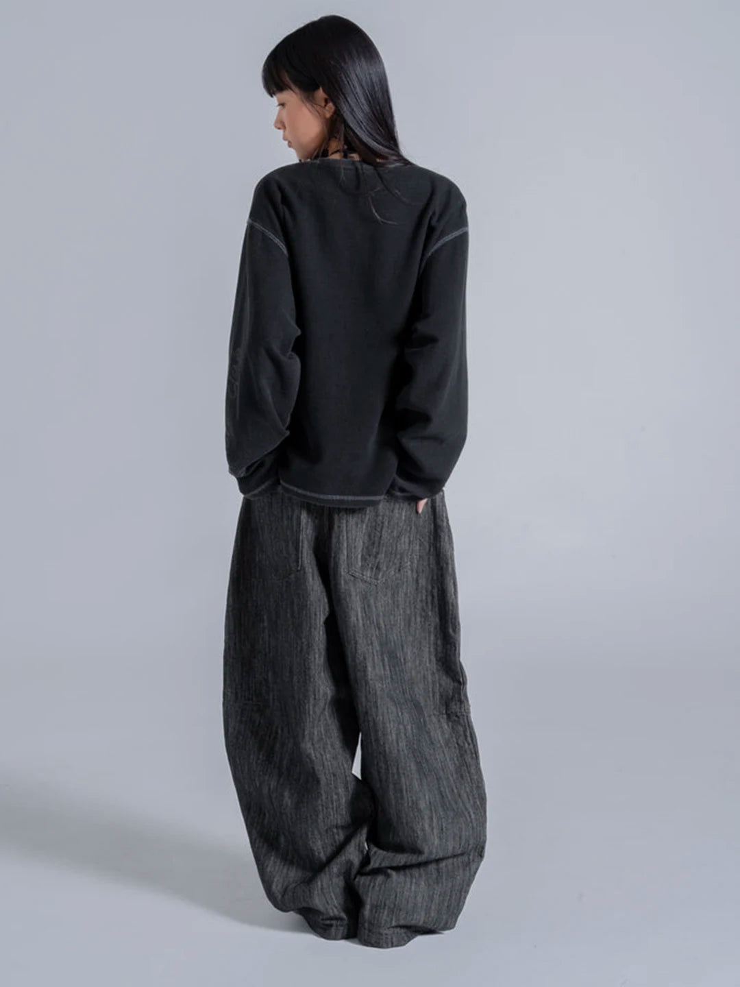 A model wearing a black long-sleeve t-shirt and wide-leg dark grey textured pants 