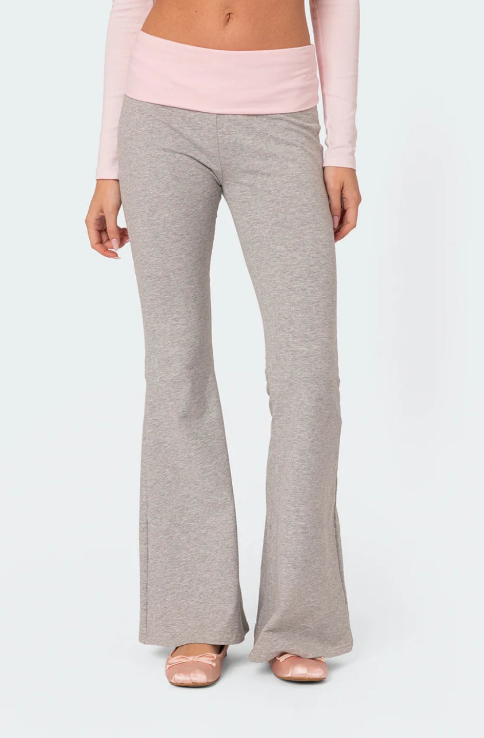 Person wearing grey flared pants and a pink top on a white background