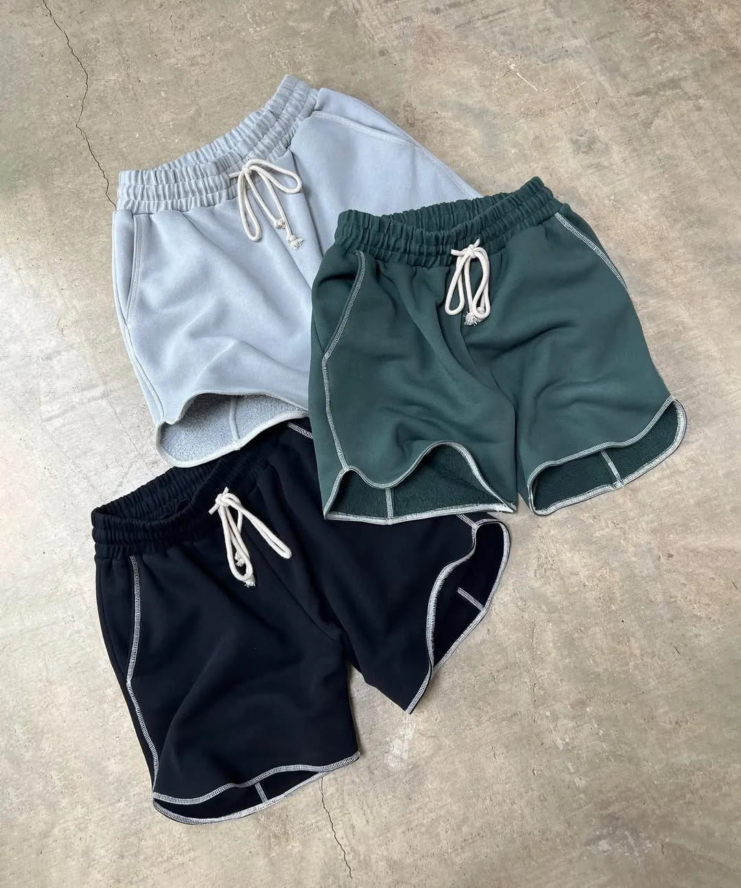 Three pairs of running shorts in grey, green, and black on a concrete floor.
