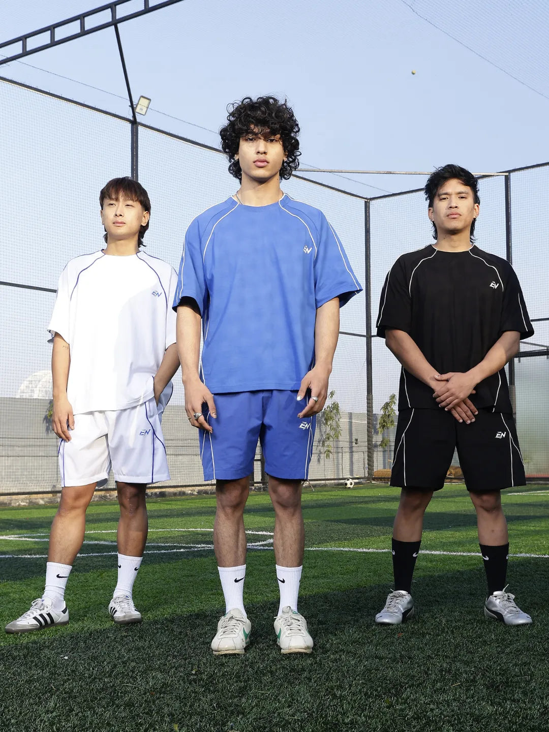 Three individuals standing on a sports field wearing athletic clothing.