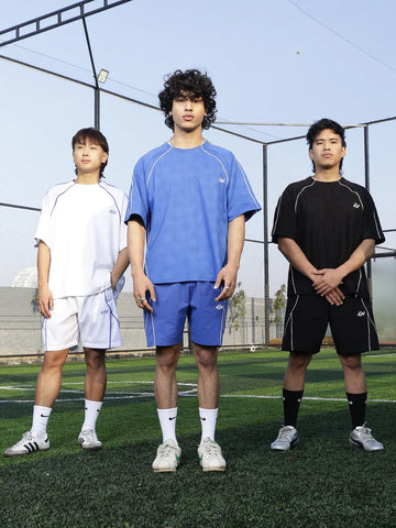 Three individuals standing on a sports field wearing athletic clothing.