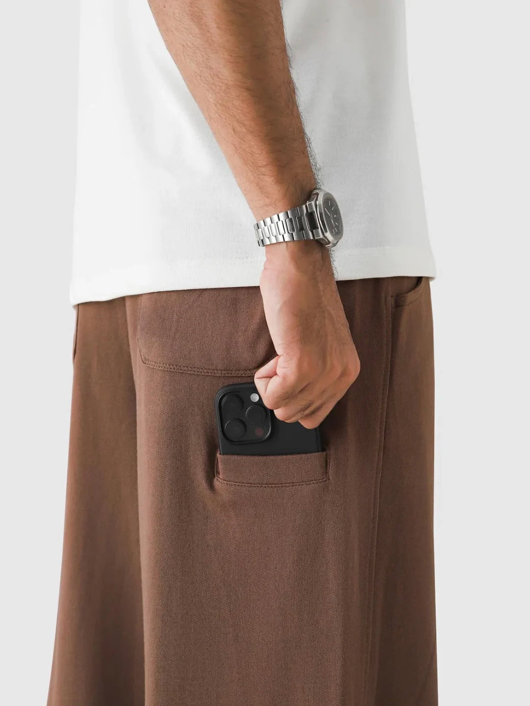 Person wearing brown pants with a pocket, holding a phone, on a plain background