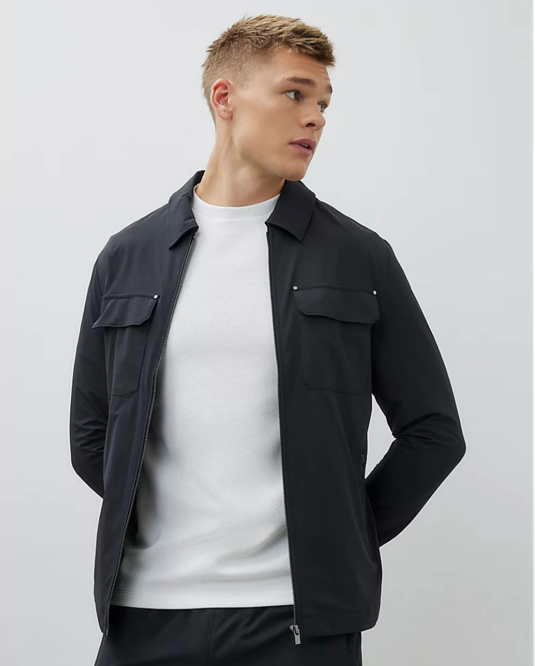 Man wearing a black jacket over a white shirt on a light gray background