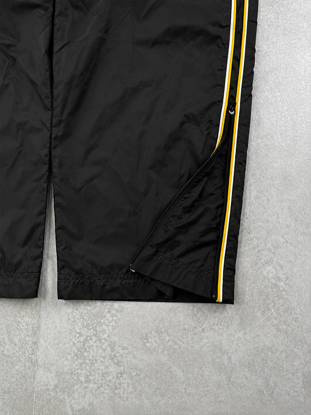 Black track pants with a red stripe and brand logo on a grey background