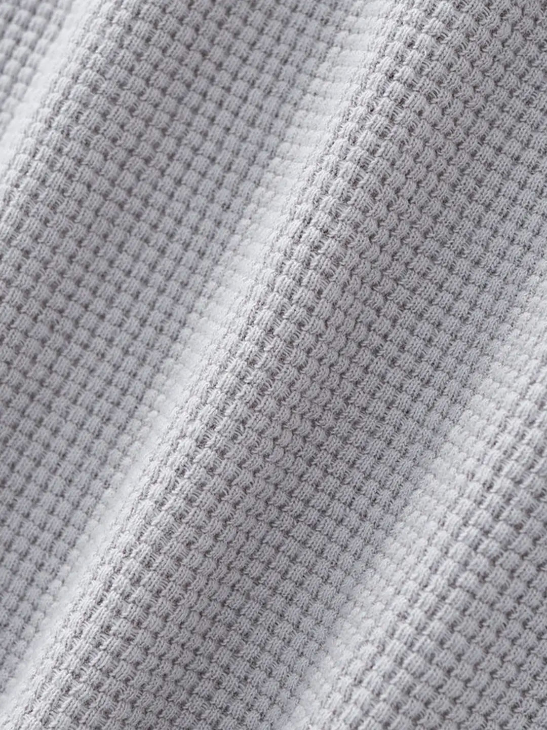 Close-up of a grey waffle-knit fabric texture with soft diagonal folds.
