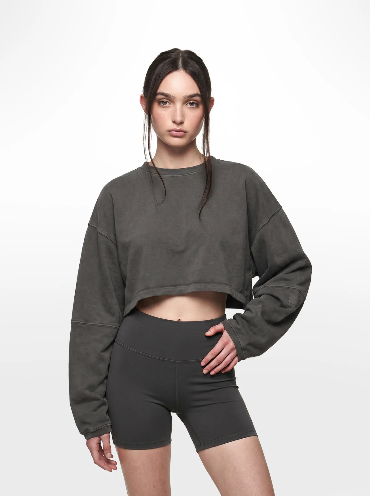 Woman wearing a dark grey cropped t-shirt and black shorts on a white background