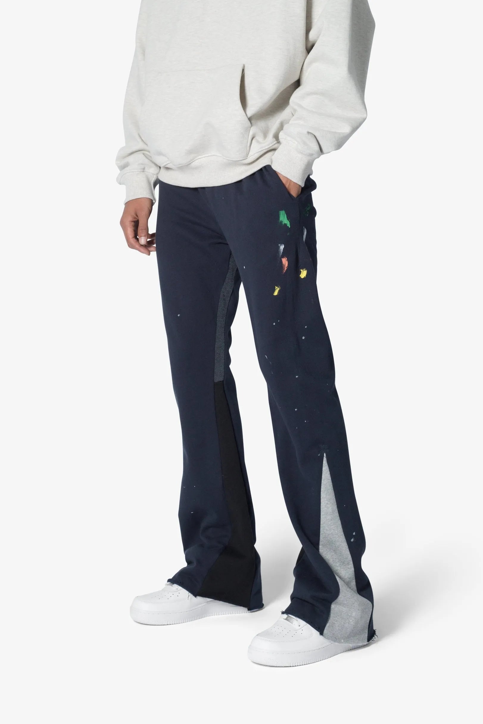 Person wearing navy pants with colorful patterns and a white sweatshirt on a white background