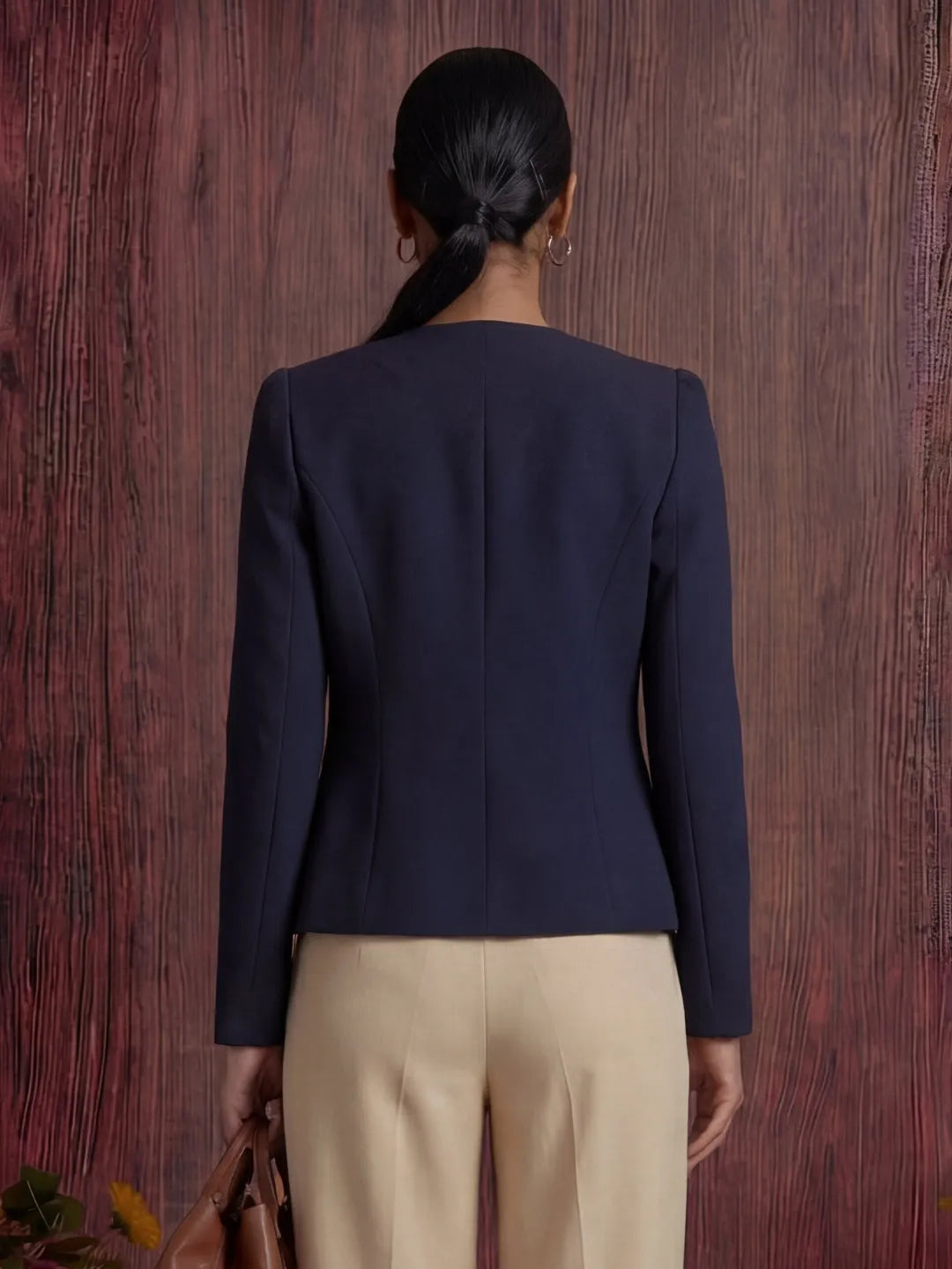 Person wearing a navy blazer and beige pants against a wooden background