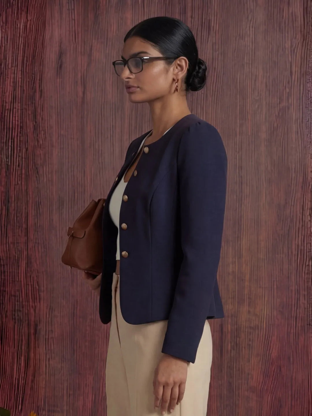 Woman wearing a navy blazer and holding a brown bag against a wooden background