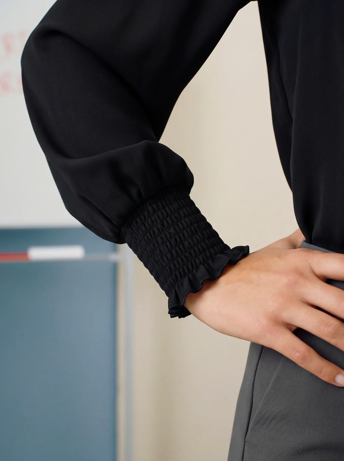 Close-up of a person wearing a black long-sleeve top with ruffled cuffs.