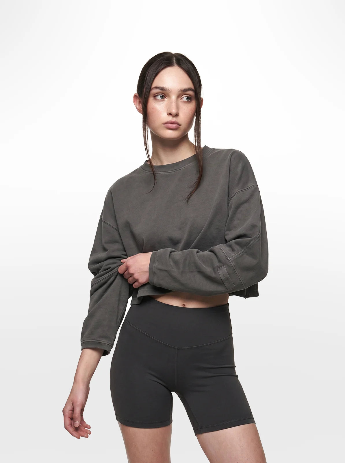Woman wearing a grey cropped t-shirt and black shorts on a white background