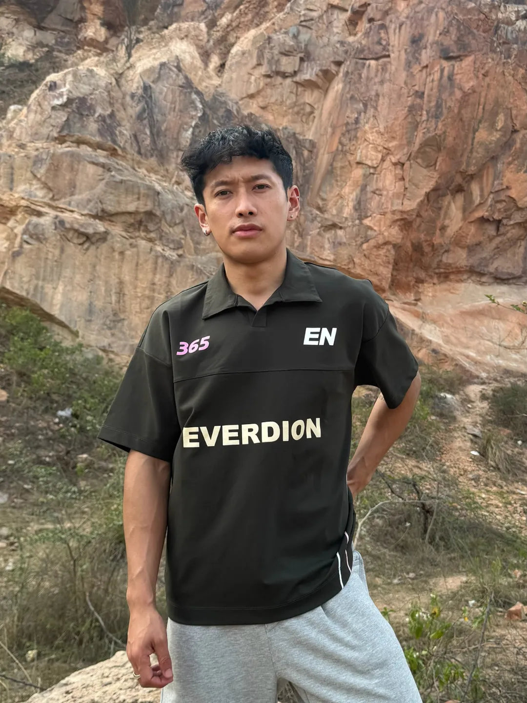 Person wearing a olive 'EVERDION' shirt standing in front of rocky terrain