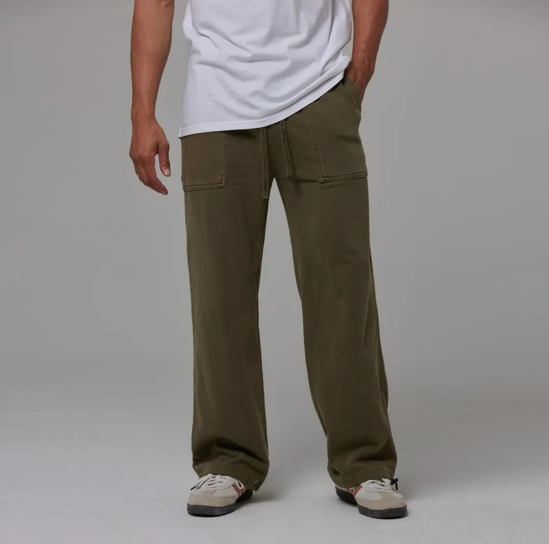Person wearing olive sweatpants and a white shirt on a grey background
