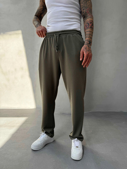 Person wearing olive green jogger pants and white sneakers in a minimalistic setting