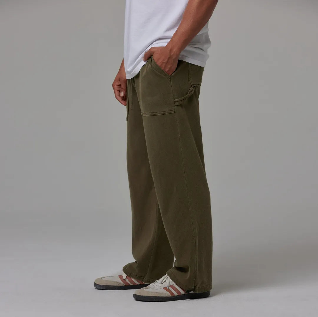 Person wearing olive sweatpants and white sneakers on a plain background