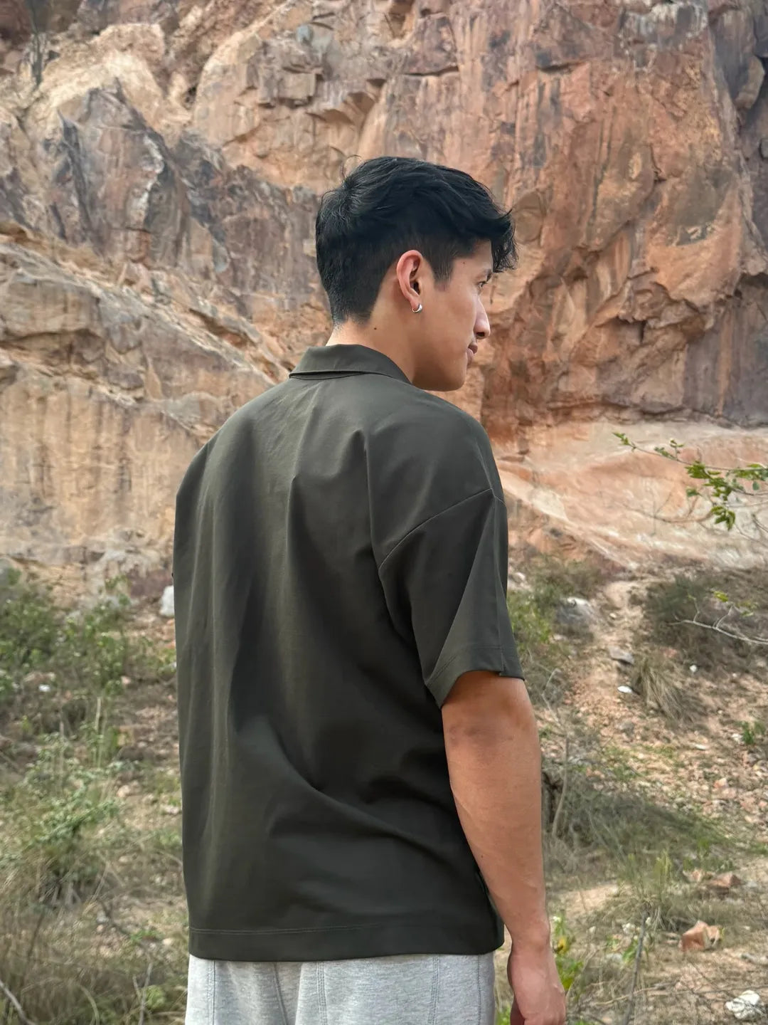 Person wearing a olive shirt standing in front of a rocky cliff
