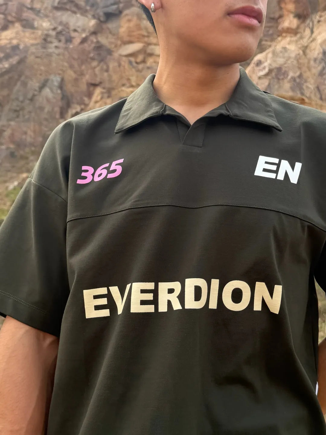 Person wearing a olive shirt with 'EVERDION' branding against a mountainous background