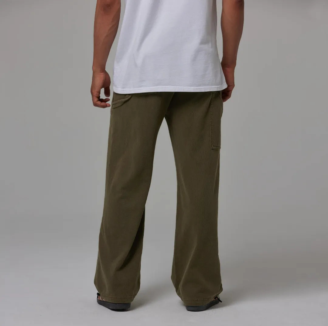 Person wearing olive green sweatpants and a white shirt on a plain background