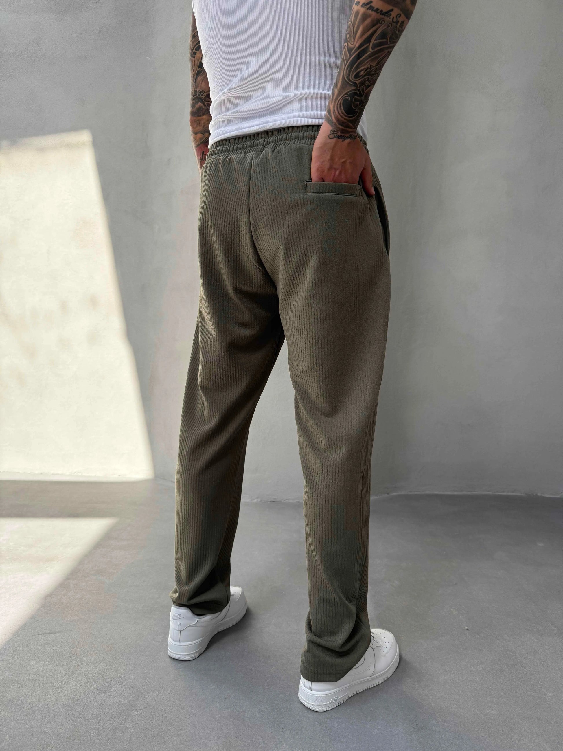 Person wearing olive green jogger and white sneakers in a minimalistic setting