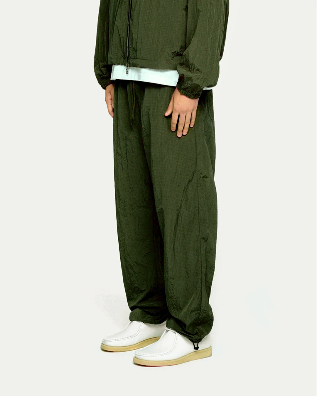 Person wearing a olive tracksuit with white shoes on a white background