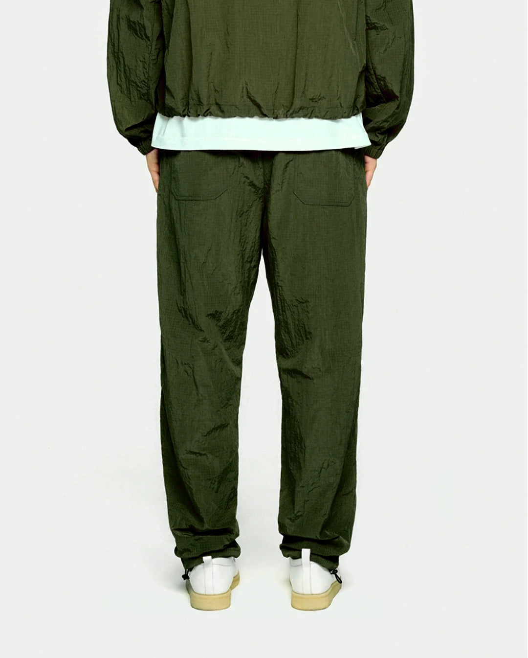 Person wearing olive tracksuit with white shoes on a light gray background