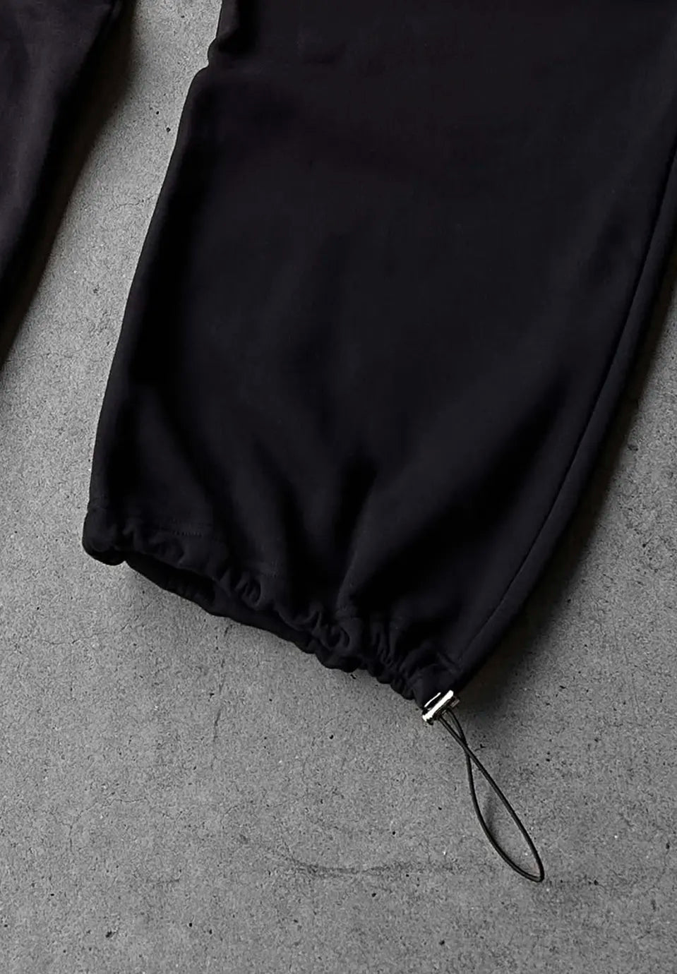 Close-up of a black drawstring pants leg with a gathered elastic cuff and a black cord loop,