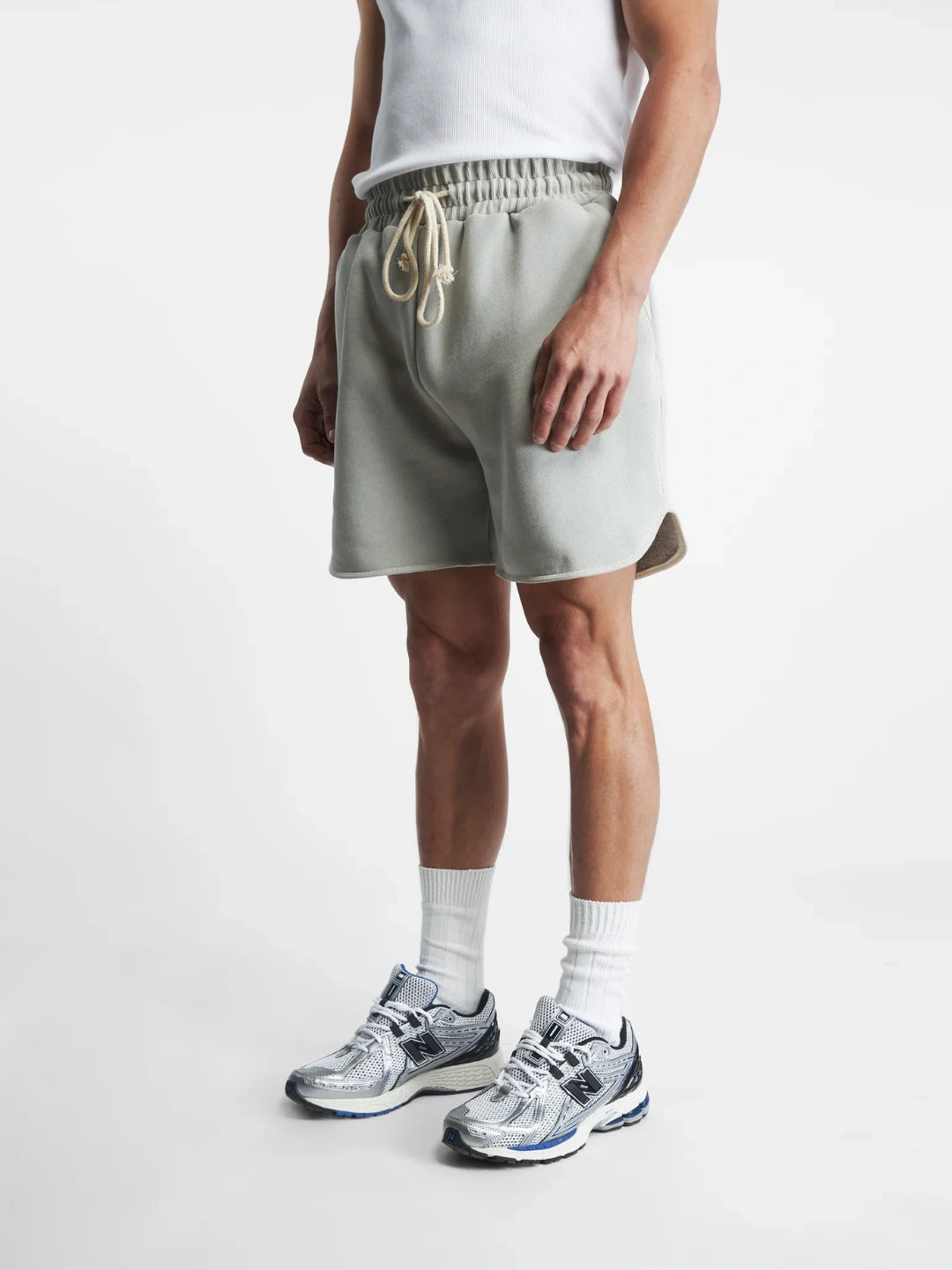 Person wearing grey shorts and white sneakers on a plain background