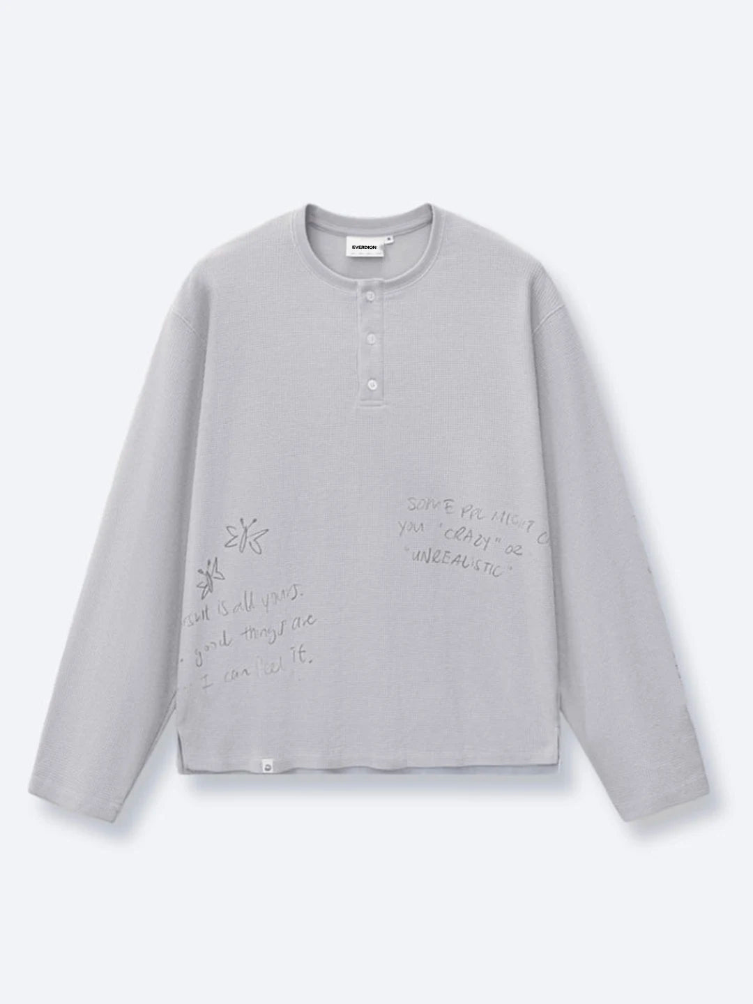 A light grey long-sleeve henley t-shirt with subtle handwritten-style text and sketch graphics printed on the front
