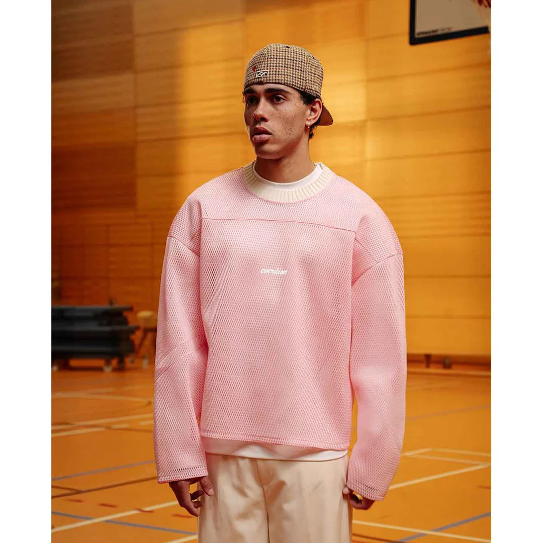 Person wearing a pink textured sweater and plaid cap indoors on a wooden floor.