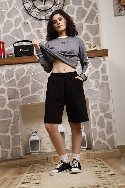Woman wearing a gray sweatshirt and black shorts standing in a room with stone walls and decorative items.