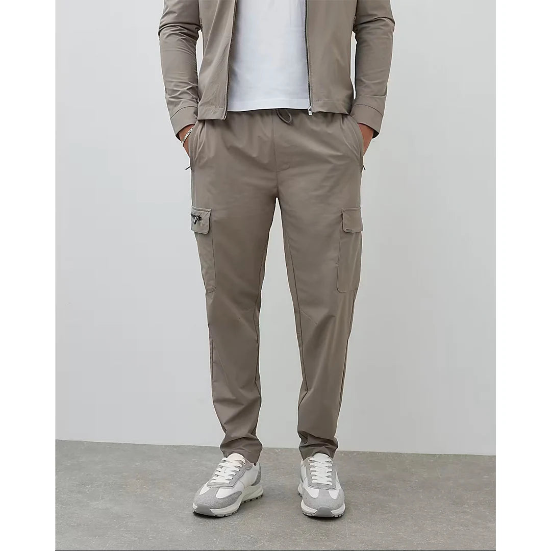 Person wearing a beige jacket and cargo pants with white sneakers on a plain background