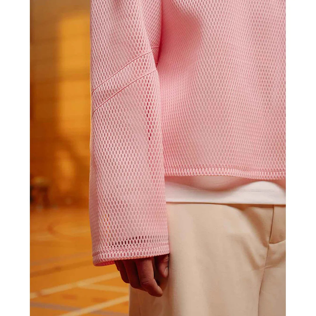 Person wearing a pink textured sweater and beige pants on a wooden floor.