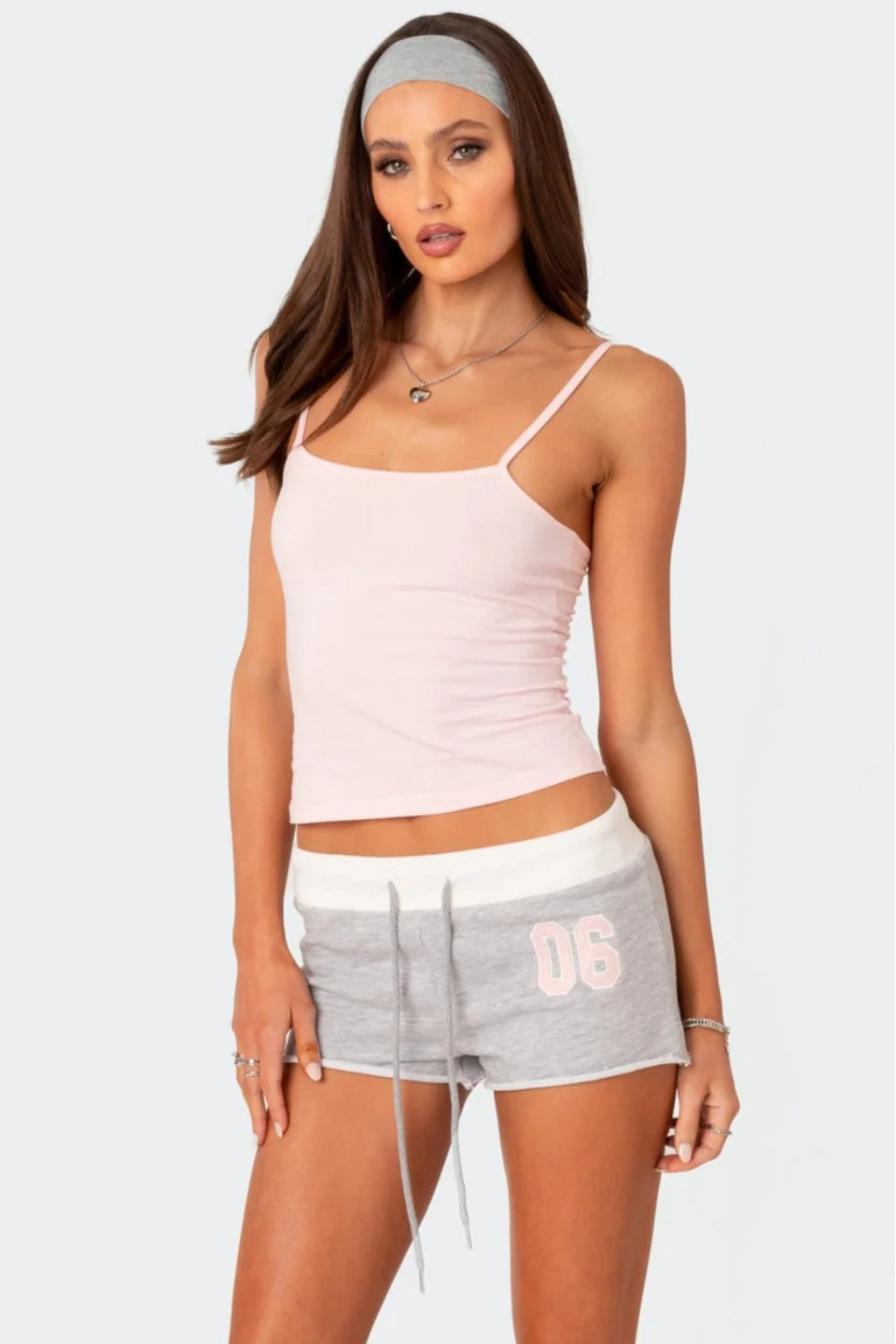 Woman wearing a light pink tank top and grey shorts with '06' on a white background