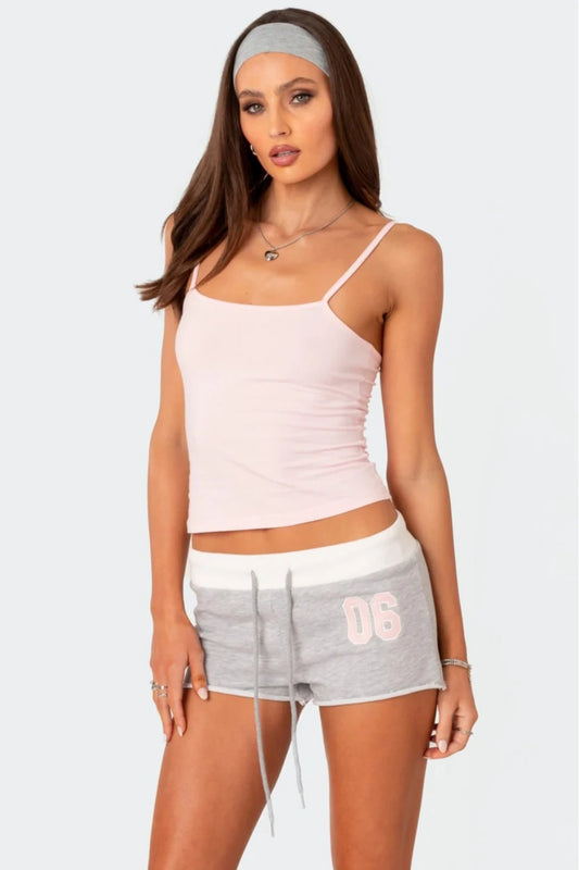 Woman wearing a light pink tank top and grey shorts with '06' on a white background