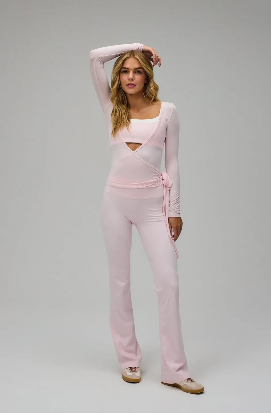 Woman wearing a light pink outfit with a cut-out design on a grey background