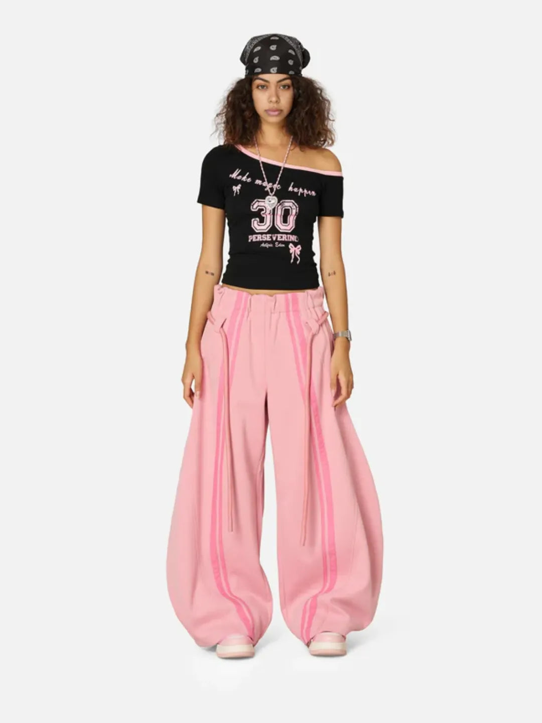 Woman wearing a black off-shoulder top with text and pink wide-leg sweatpants on a white background
