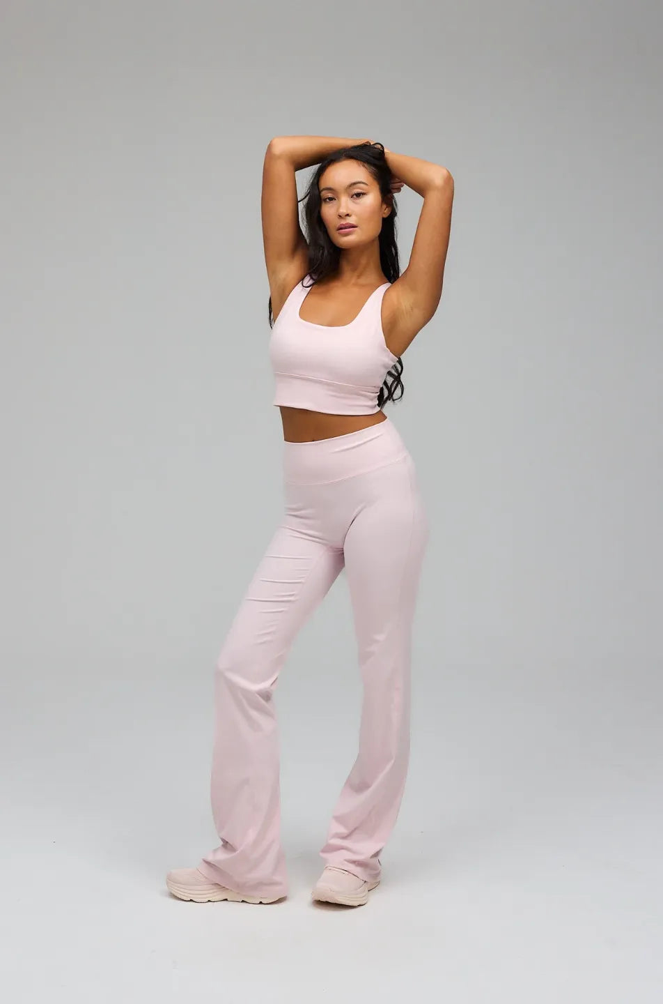 Woman wearing a pink athletic outfit posing against a grey background