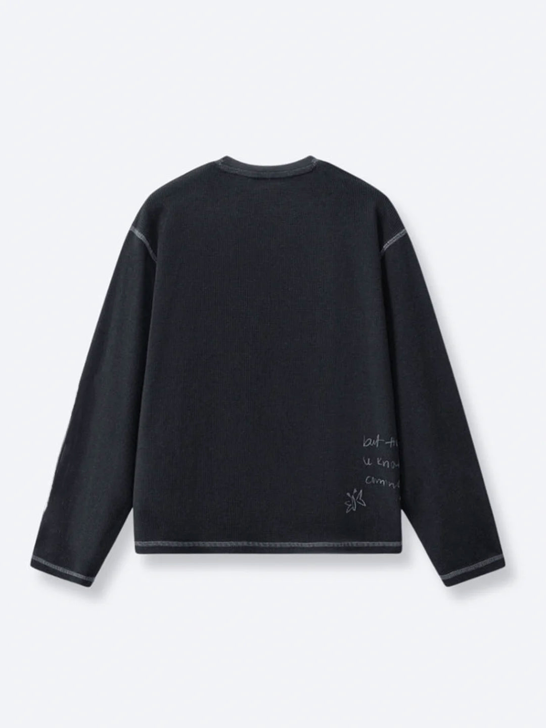 A black long-sleeve crewneck tshirt featuring subtle grey contrast stitching and small white handwritten-style text and sketch graphics on the lower right back