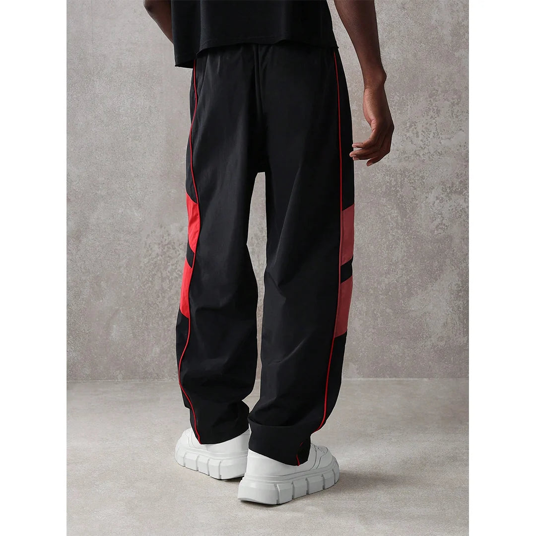 Person wearing black pants with red stripes and white sneakers on a gray background