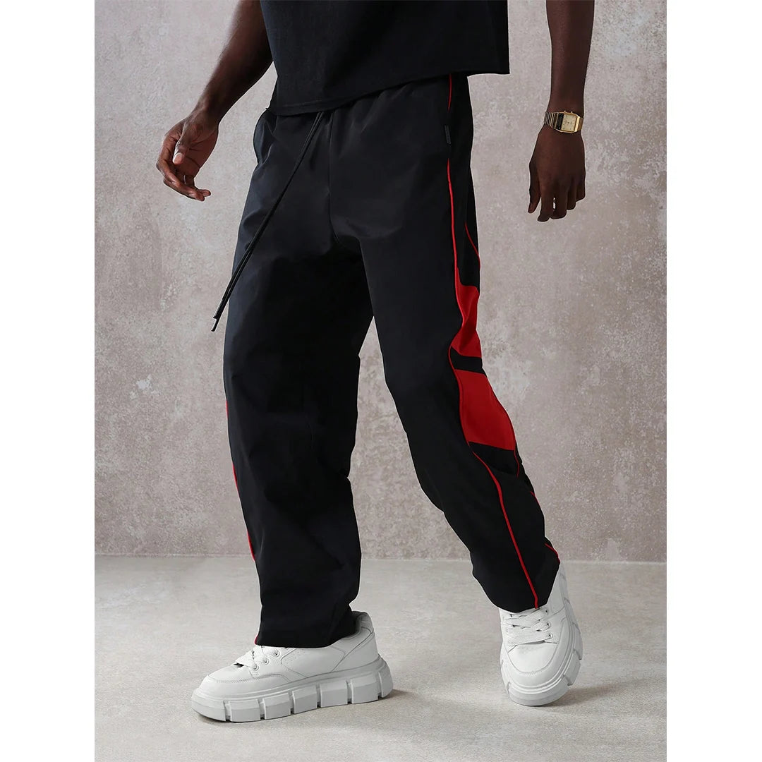 Person wearing black jogger pants with red stripes and white sneakers against a gray background