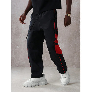 Person wearing black jogger pants with red stripes and white sneakers against a gray background
