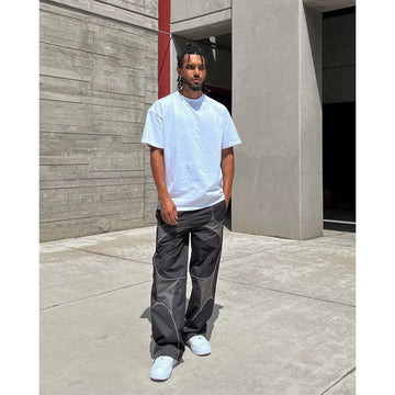 Person wearing a white t-shirt and gray pants standing in front of a concrete wall.