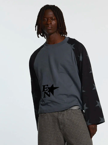A model wearing a dark grey and black raglan long-sleeve shirt with a black star graphic on the chest and star-patterned sleeves, paired with gray plaid trousers