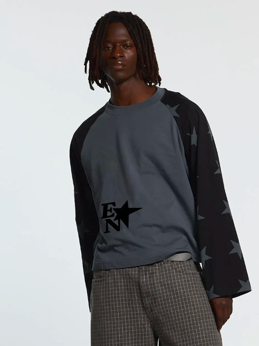 A model wearing a dark grey and black raglan long-sleeve shirt with a black star graphic on the chest and star-patterned sleeves, paired with gray plaid trousers