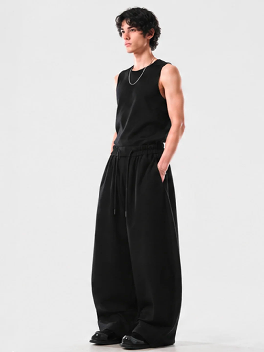 Person wearing a black sleeveless top and wide-leg sweats on a white background