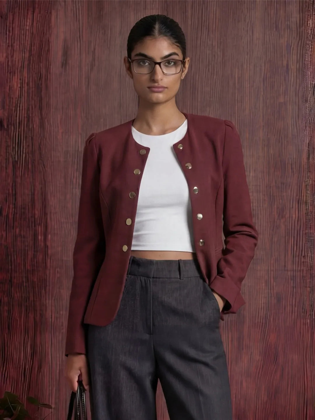 Person wearing a burgundy jacket over a white top and dark pants against a wooden background