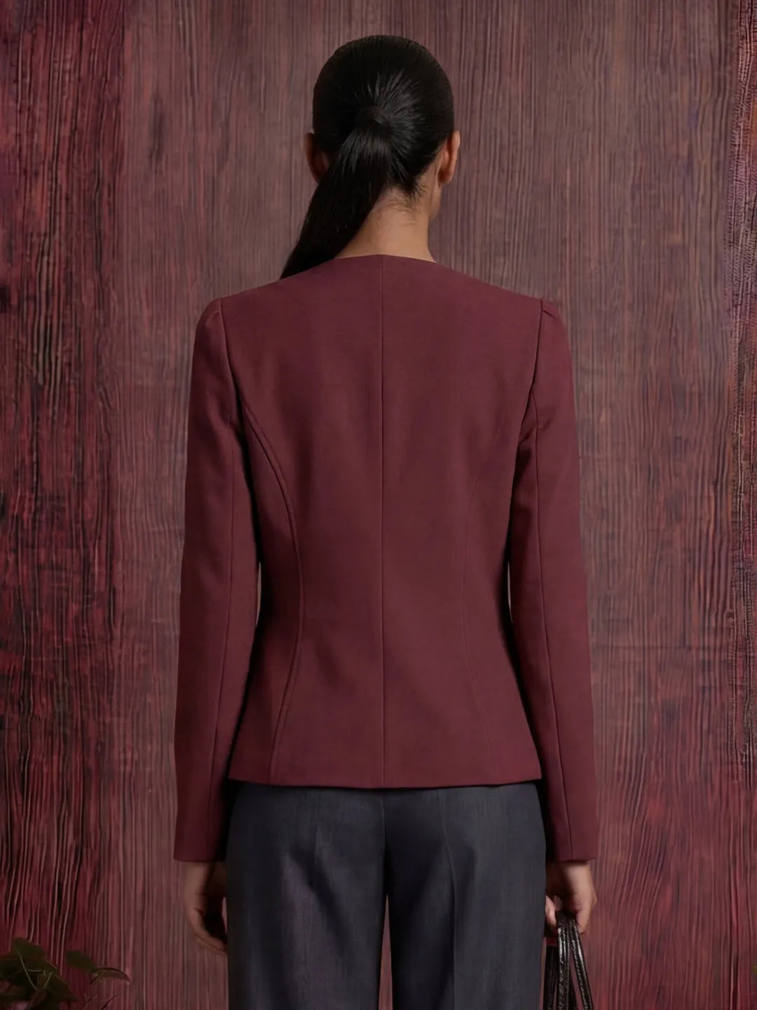 Person wearing a burgundy blazer against a wooden background