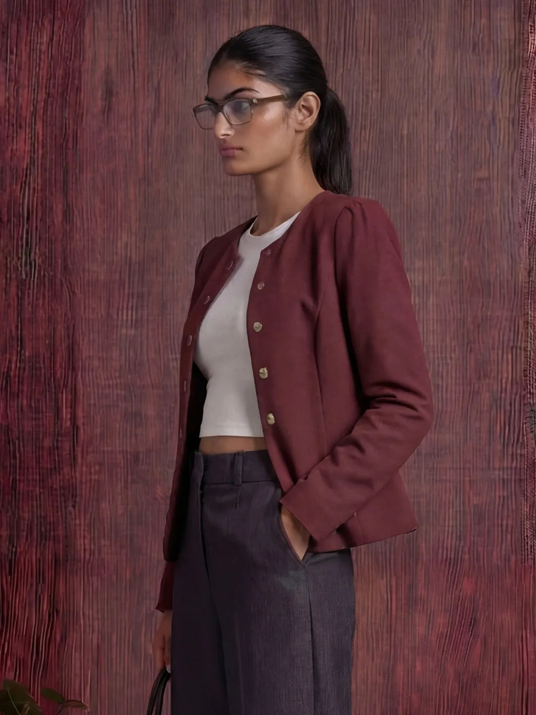 Woman wearing a burgundy blazer over a white top and dark pants against a wooden background