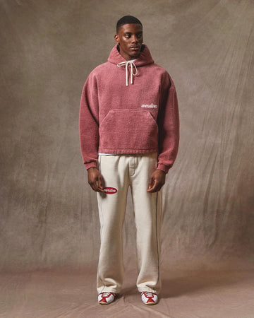 Person wearing a red hoodie and white pants against a brown background