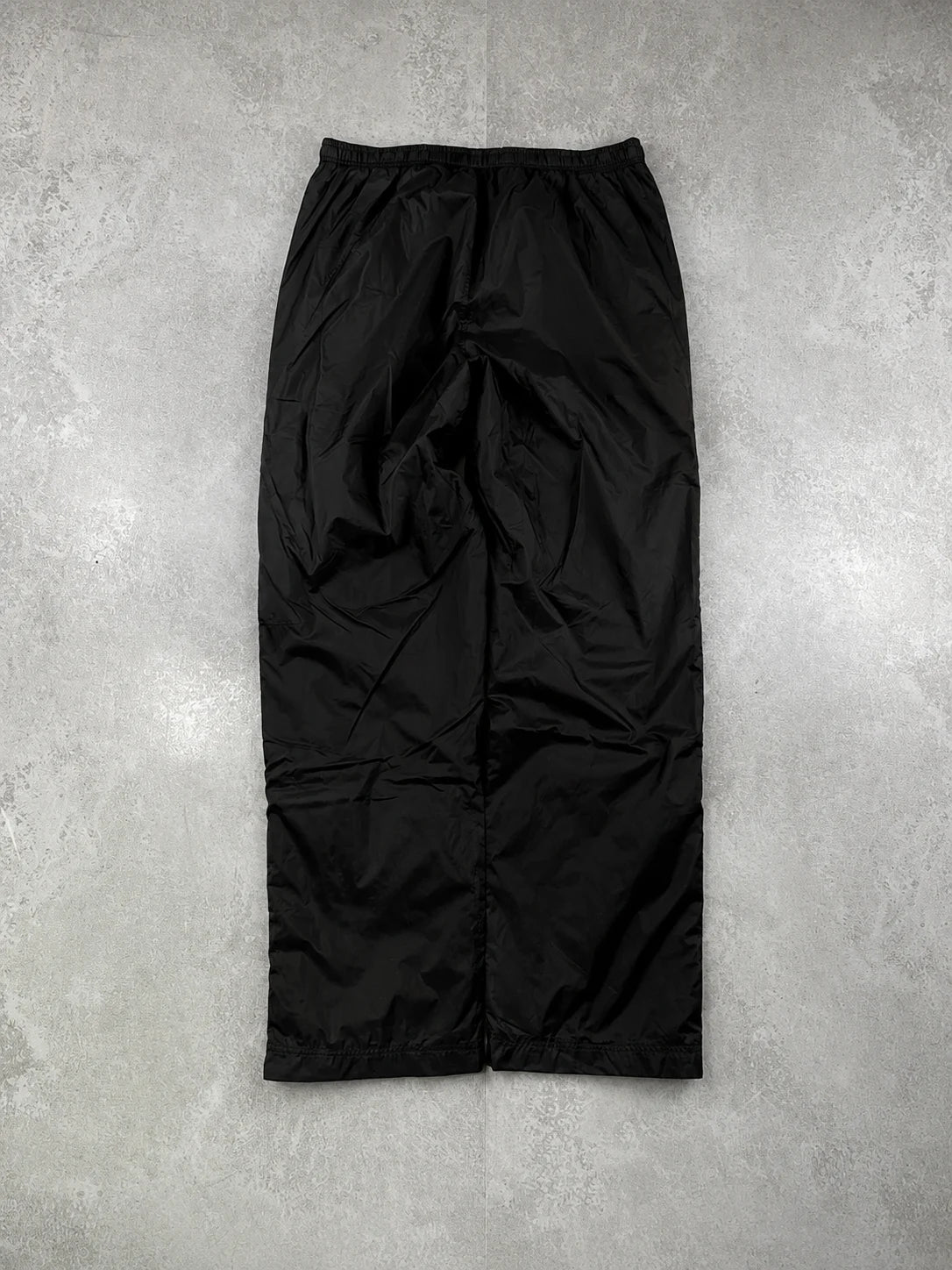 Black track pants with a red stripe and brand logo on a grey background